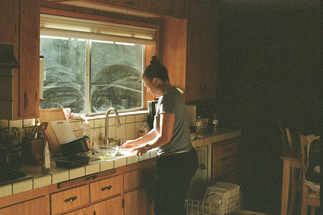 A man cleaning a glass door indoors using a spray bottle and cloth.